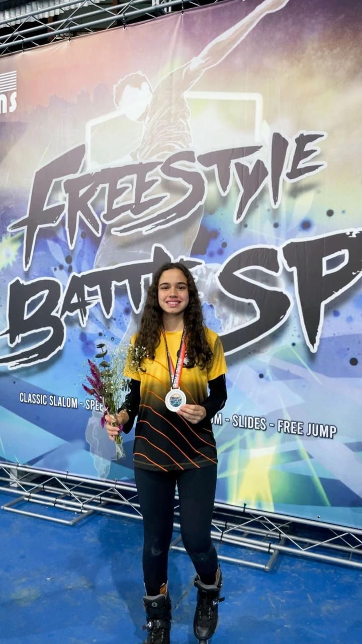 Yasmin sorrindo com a medalha de prata no pescoço e um buquê na mão