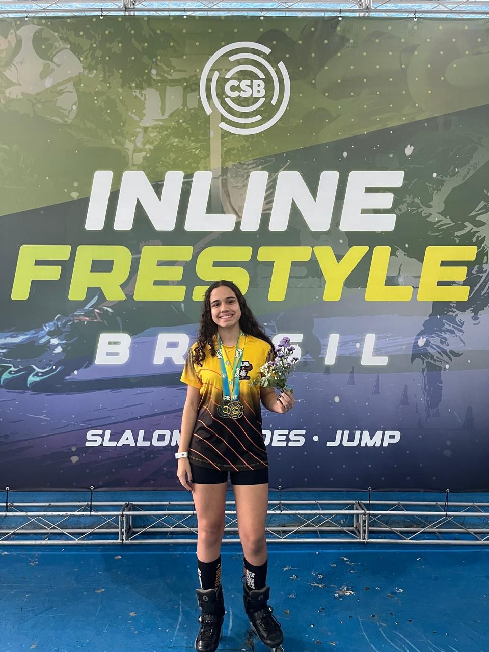 Yasmin com a medalha de ouro em frente ao painel do Inline Freestyle Brasil